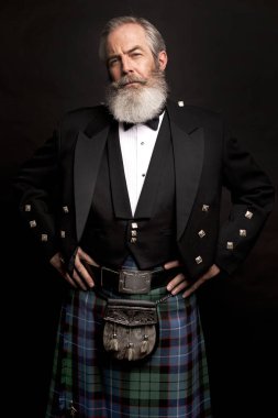 close up of senior man with grey hair and full beard, wearing scotting kilt on dark background clipart
