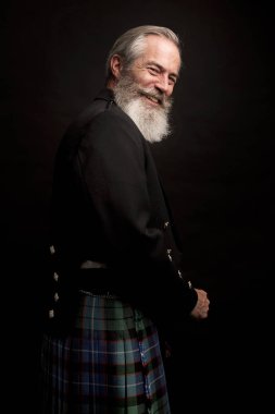 close up of senior man with grey hair and full beard, wearing scotting kilt on dark background clipart