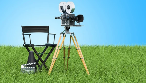 Cinema concept. Movie camera with film reels, chair, megaphone and clapperboard on the green grass against blue sky, 3D rendering