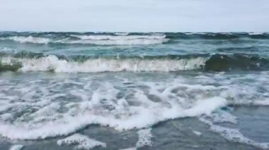 Rüzgarlı dalgalar kumlu bir sahil üzerinde çalışan.