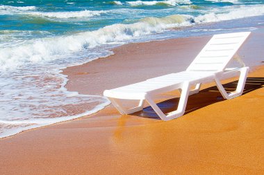 Deniz tarafından kumlu bir plajda duran beyaz şezlong