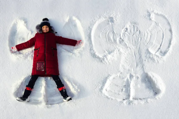 A menina está na neve e faz um anjo da neve Imagem De Stock