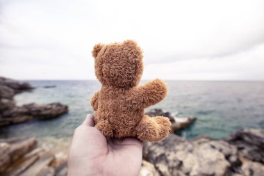 Çocuk oyuncak - deniz arka plan üzerinde avucunun içinde bir oyuncak ayı. Yalnızlık veya nostalji ile ilgili yayınlar göstermek. Kavram-hayalleri gerçek oldu.