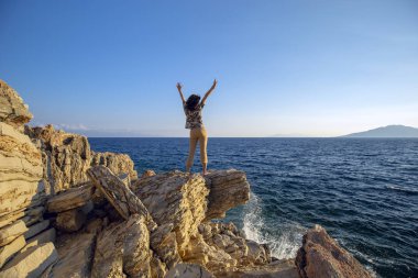 Yalnızlık denizin kenarında vahşi bir plajda tadını çıkarın. Kadın ellerini kaldırdı ve gün batımında denize baktı.