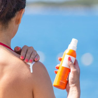 Orta yaşlı bir kadın için güneş cildi korur. Onun elinde o bir tüp güneş kremi tutar.