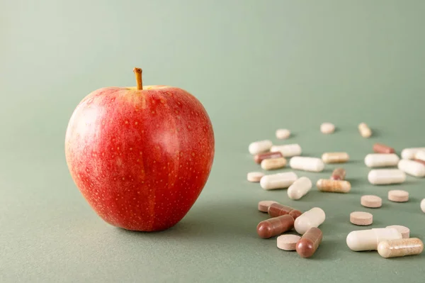 In the picture there is apple vs pills. This is the concept of the health benefits of eating fruits. Natural vitamins against pills for health benefits.
