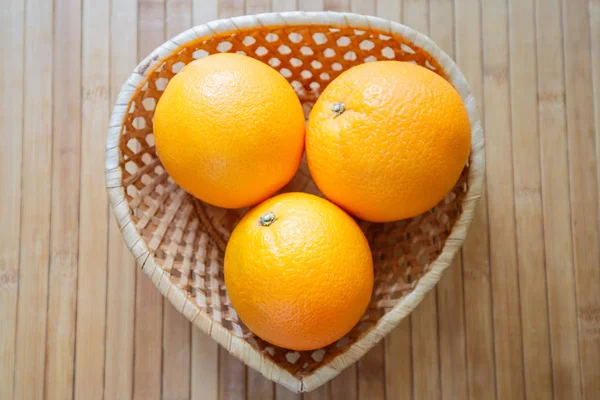A fruit basket with three succulent oranges. A basket in the shape of a heart as a symbol of health benefits.
