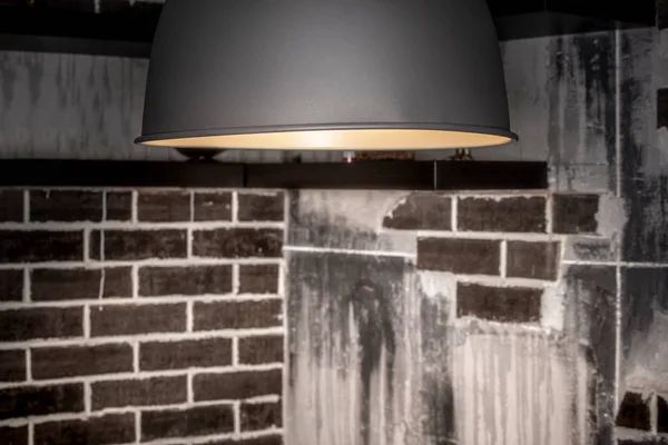 In the attic, a lamp with a metal lampshade is lit. Texture of brick walls and concrete areas. Concept design thinking.