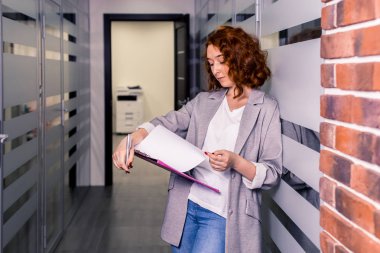 Kavram - ofis, adet eser bulunmaktadır. Bir kız bir ceket ve kot ofis koridorunda bir rapor okuyor