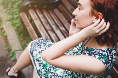 Bir cep telefonuna bir parkta bankta Kızıl saçlı bir kızla konuşuyor.