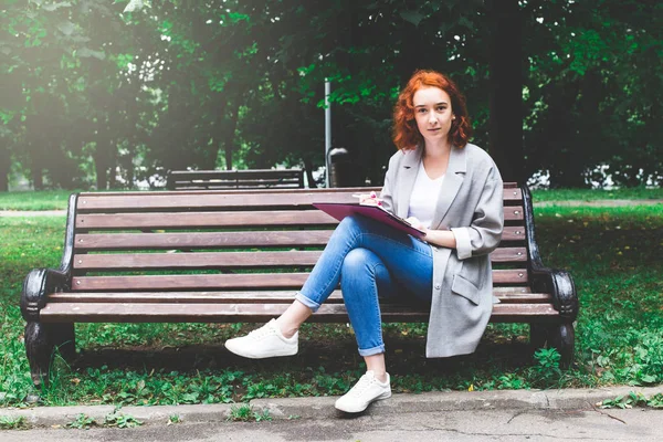 女孩与红色头发铅笔素描在公园长椅上 — 图库照片