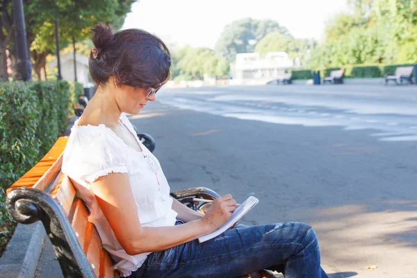 一位中年妇女坐在公园长椅上 那个黑发女孩城市公园的休息食谱 — 图库照片