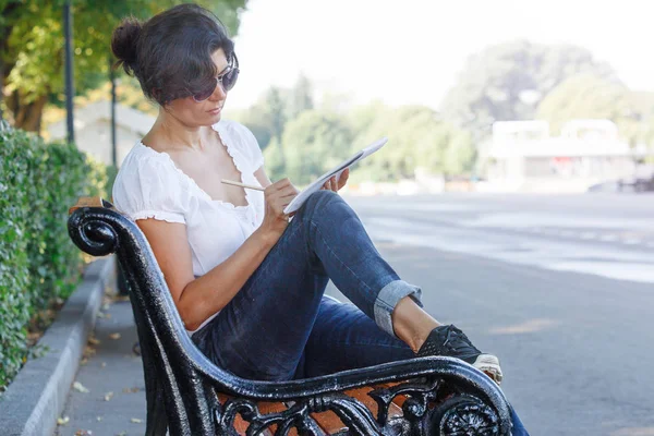 那个女孩在公园长椅上的笔记本上写字 身穿蓝色牛仔裤和白色上衣的中年黑发妇女 — 图库照片