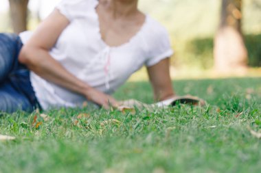 Bir kız parkta okuyor. Sakin ruh hali ve gevşeme yeşil çimenlerin üzerinde bir parkta bir kavram. Mavi Jeans orta yaşlı bir kadın.