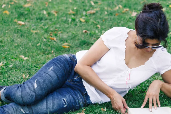 一个女孩在公园里看书 在绿色草地上的公园里平静的心情和放松的概念 穿着蓝色牛仔裤的中年妇女 — 图库照片