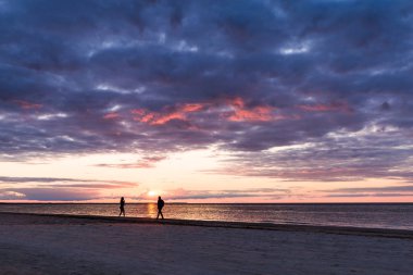 Erkek ve kadın sahilde. Gün batımında insan siluetleri. Baltık Denizi.
