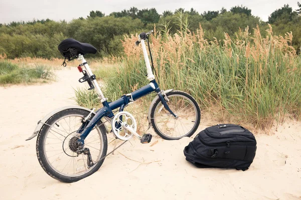 The concept of traveling on a bike as a way to preserve the ecology. A bicycle and a backpack on the sand of the beach.