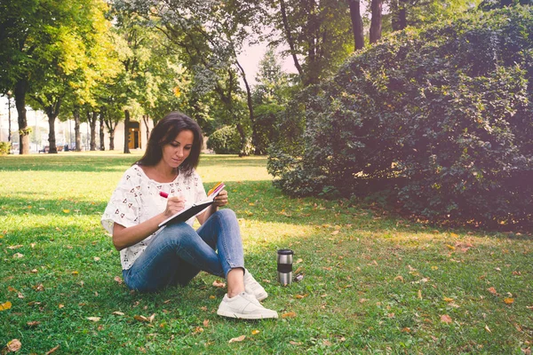 一位中年妇女在贴纸上写了一个标记 概念设计思想 一个穿着牛仔裤的女孩坐在夏日公园的草地上 — 图库照片