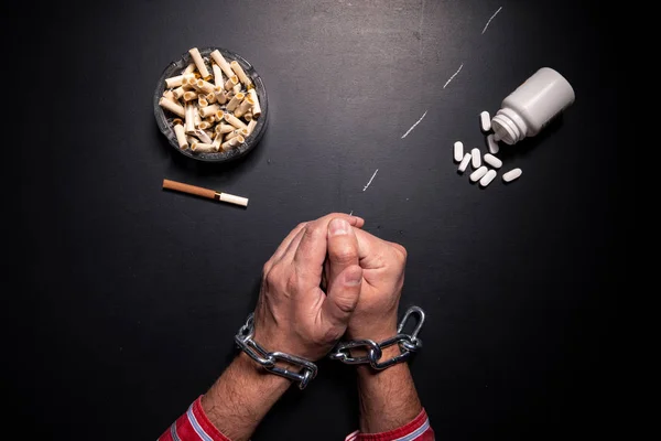 The concept of smoking and harm to health. An ashtray and a cigarette on a black board and white medical pills. Chained hands are a sign of nicotine addiction.