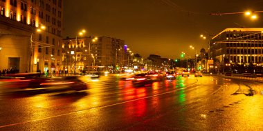 Gece şehir ışıkları yağmur altında. Arabalar hareket ve bulanık. Dış aydınlatma.