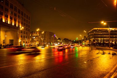 Gece şehir ışıkları yağmur altında. Arabalar hareket ve bulanık. Dış aydınlatma.