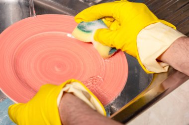 Bir adam bir temizlik maddesi ile mutfakta bulaşık yıkar.