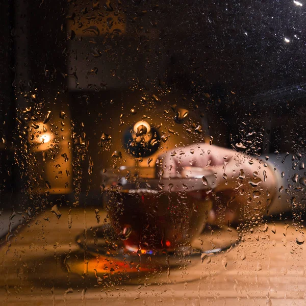A cup of hot tea in wet weather. Drops of water on the glass in a rainy evening.