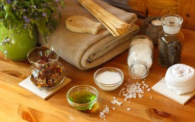 Banyo havlusu, bambu süpürgesi ve doğal şampuanlar, kokulu tuz ve ahşap bir masada bir sürahi çiçek.