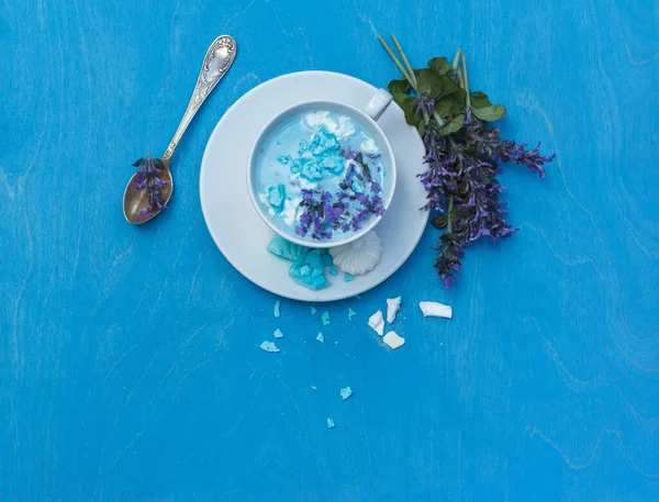 A Cup of blue moon milk, an Ayurvedic natural soothing drink for healthy sleep, with blue flowers and meringue. top view with space on a blue background