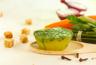 Kek şeklinde donmuş yeşil et suyu, ahşap kaşıkta baharatlar ve sebzeler. Arka planda yemek pişirmek için sebzeler, bulanık. Yatay olarak uzayla