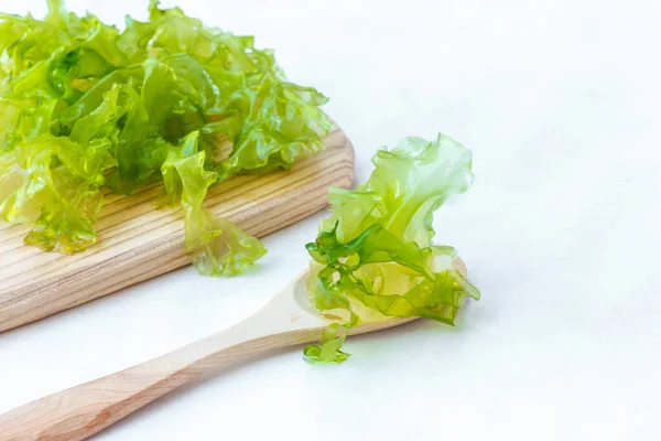 Свежие зеленые листья водорослей, для приготовления салата, на деревянной доске, светлый фон, горизонтально — стоковое фото