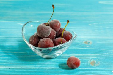 Mavi ahşap arka planda cam bir kasede donmuş kiraz, yatay olarak, kapat. Boşlukları kopyala