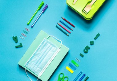 Okul için ofis malzemelerinin mavi arka planında düzlük, bir beslenme çantası ve koruyucu bir maske. Yatay yönelim