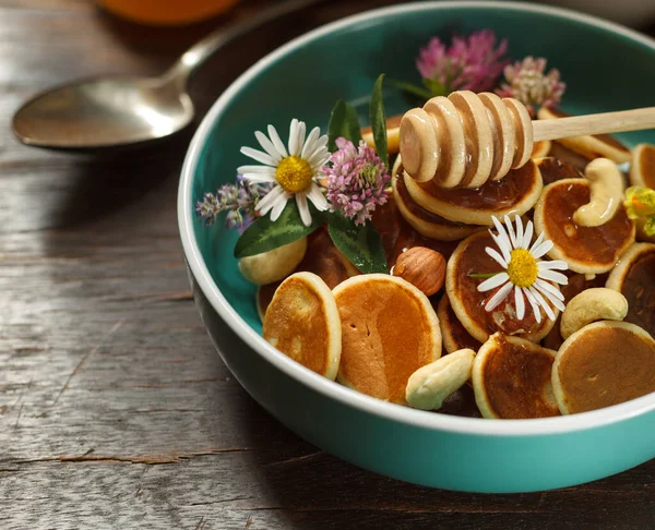 Mini panqueques en un tazón azul con nueces y miel, decorado con flores frescas. — Foto de Stock