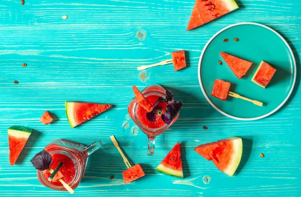 Bardakta kırmızı fesleğenli karpuz püresi ve akuamarin ahşap arka planda kırmızı karpuz dilimleri..