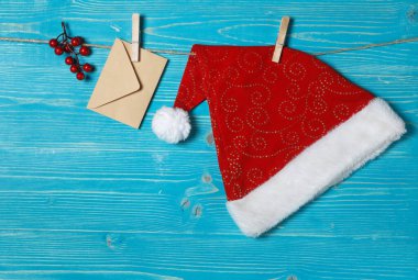 Noel Baba şapkası ve el işi kağıt bir zarf. Çamaşır mandalında, çamaşır ipinde yazı için yer var. Mavi ahşap zemin, yatay çerçeve