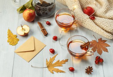 İki bardak mis kokulu çay, hafif tahtalarda gül kalçası ve baharatlar, bir çelenk, elmalar ve kuru yapraklar.