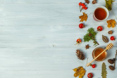 Gri ahşap arka planda sonbahar kompozisyonu kuru yapraklar, gül ağacı çayı, bal kavanozları, kırmızı böğürtlen. Üst görünüm, yatay, boşluklu