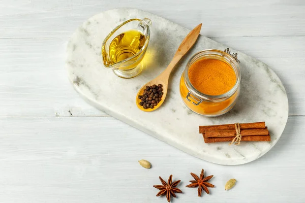 Cúrcuma molida, pimienta negra, aceite vegetal y palitos de canela en un soporte de mármol. Cerrar - sobre un fondo de madera claro con espacio — Foto de Stock