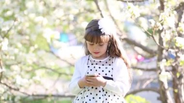 Beyaz elbiseli bir kız küçük ses kulaklık aracılığıyla müzik dinler. Güzel bir kız bir yaz bahçesinde kendini telefondan bir ses kulaklık kulağına koyar.
