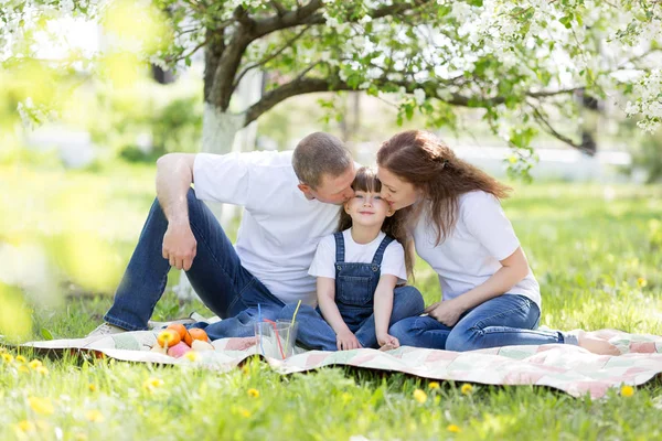 Parents kiss their beautiful daughter sitting under a tree.