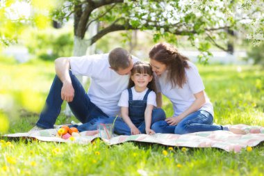 Mutlu aile ile bir yaz parkta beyaz bir köpek. Veliler ve 5 yaşındaki kızı bahçe çiçek açması bir elma ağacının altına oturma.