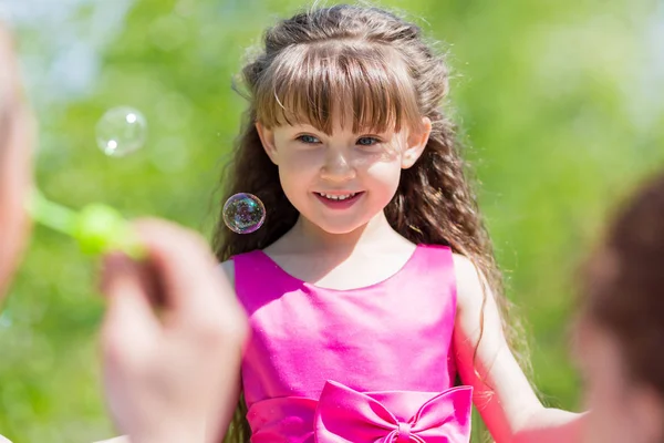 Parents let the soap bubbles on their daughter in the summer in the park. Little girl is playing with soap bubbles.