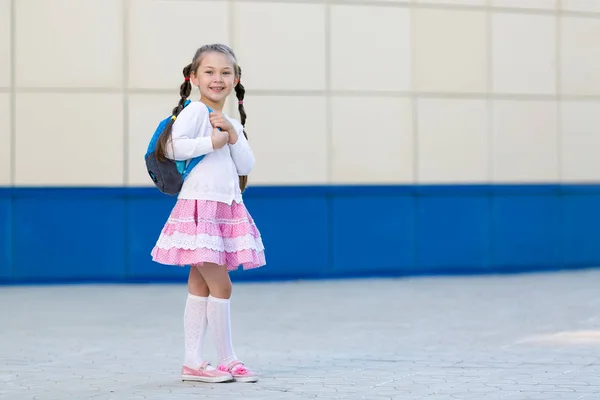 一个穿着书包的小漂亮女孩正站在城市的墙边 — 图库照片