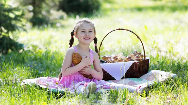 A little girl bites bread from her hands in the summer on a picnic in a city park.