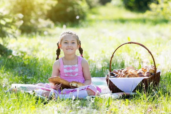 A little girl bites bread from her hands in the summer on a picnic in a city park. A child is eating bread sitting on the grass.