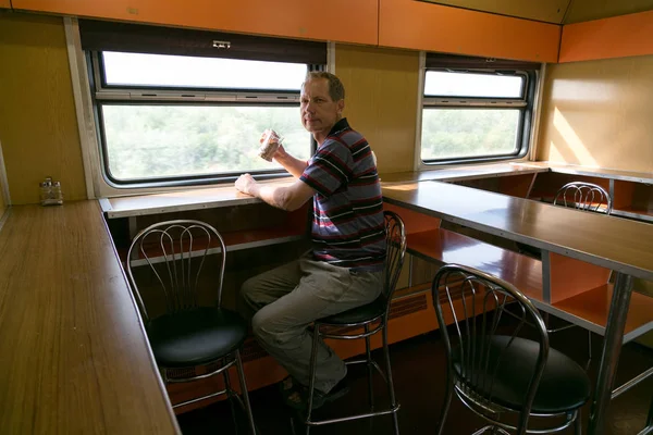 A man 40 - 50 years old is drinking tea in a long-distance train. A man is riding in a train restaurant.