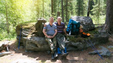Yolcuları ormanın içinde büyük bir kayanın üzerinde oturuyorsun. İki turist kardeşler dinlenme dağlarda uzun bir yürüyüş sırasında orman.