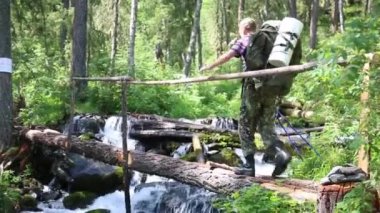 Bir kişi, bir oturum açma için nehir haçlar. Bir turist derme çatma bir köprü bir dağ dere geçer.
