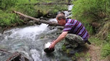 Bir adam bir dağ nehir su alıyor. Yürüyüşe yemek pişirmek için su ile pan turist doldurur.